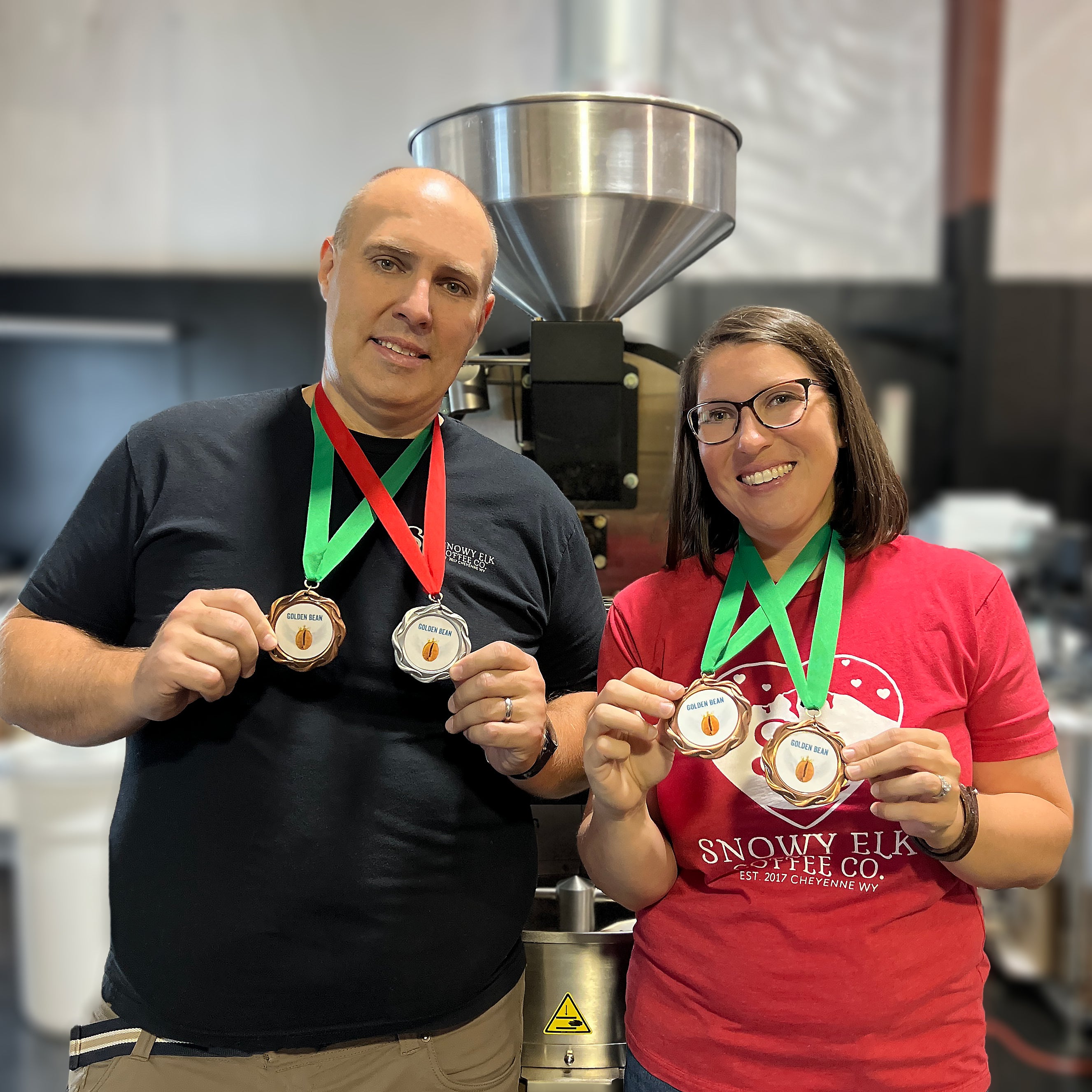 Owners, Scott and Julie, holding Golden Bean medals in front of coffee roaster
