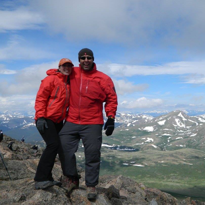 A couple wearing red jackets standing on top of a mountain