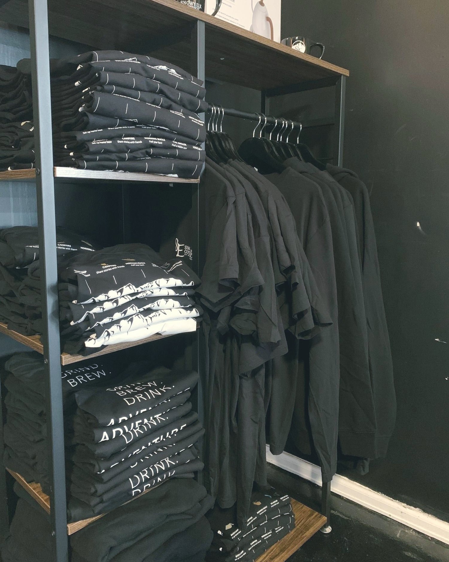 A clothing rack with folded black shirts and black shirts on hangers