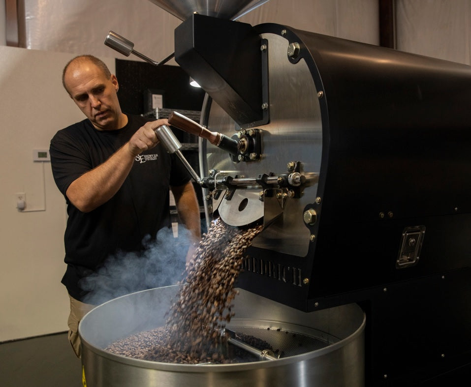 Man standing near an industrial coffee roaster while beans pour into the cooling bin