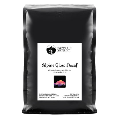 A bag of Snowy Elk Coffee Co. Alpine Glow Decaf, showing the coffee packaging with a mountain logo, a depiction of a deer, and the Swiss Water Process label.
