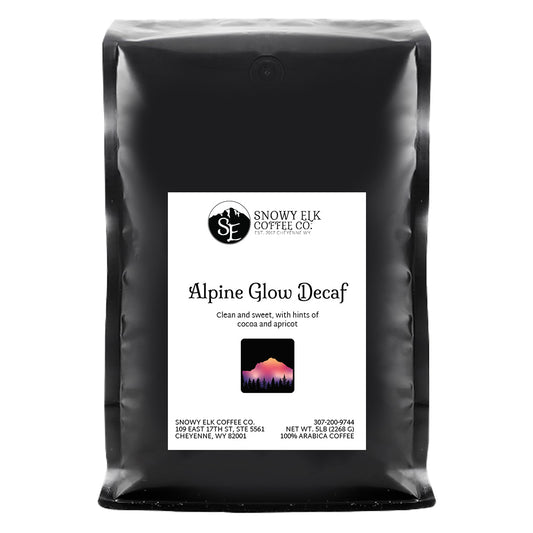 A bag of Snowy Elk Coffee Co. Alpine Glow Decaf, showing the coffee packaging with a mountain logo, a depiction of a deer, and the Swiss Water Process label.