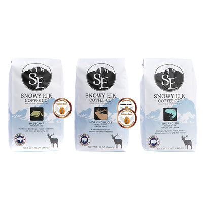 Three bags of Snowy Elk coffee, featuring light, medium, and dark roast, arranged side by side against a white background.