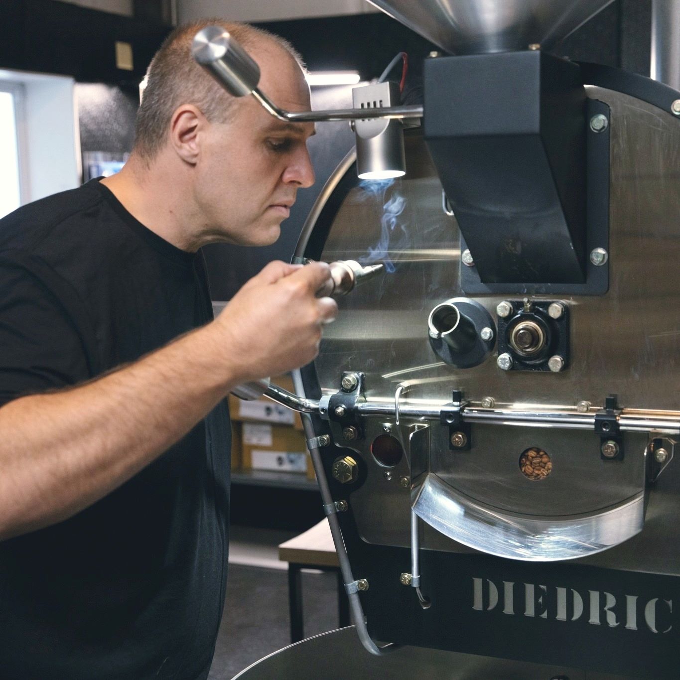 Man smelling fresh roasted beans near an industrial coffee roaster