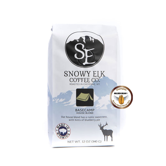 A white and blue bag of BaseCamp coffee with Snowy Elk branding and a green tent logo on the front A white and blue bag of BaseCamp coffee with Snowy Elk branding and a green tent logo on the front